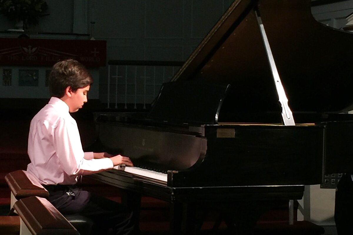 A piano student performing on a grand piano at a recital