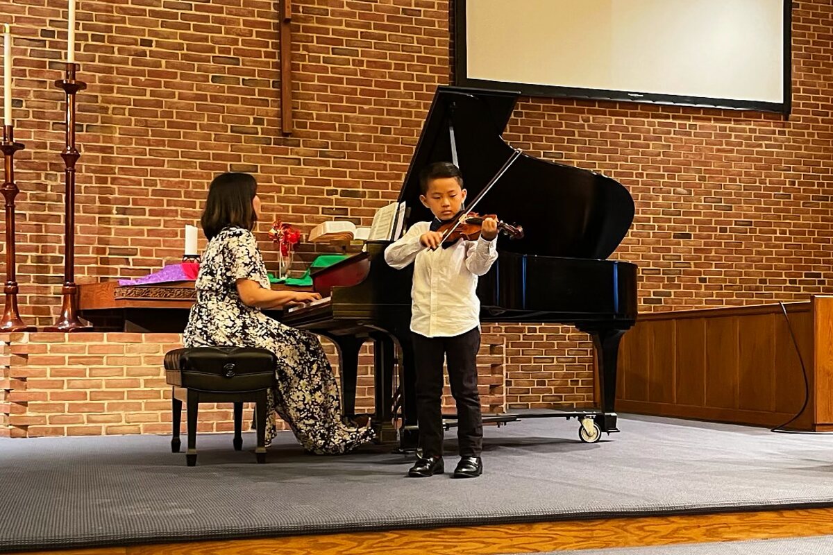 A young violin student performing on stage with a piano accompanist